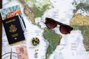 Flat lay of travel essentials with a world map, passport, and sunglasses.