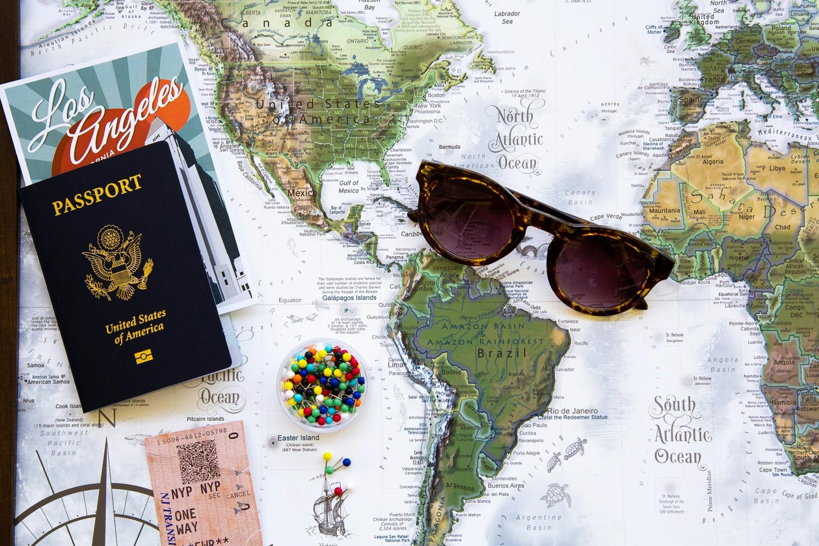 Flat lay of travel essentials with a world map, passport, and sunglasses.